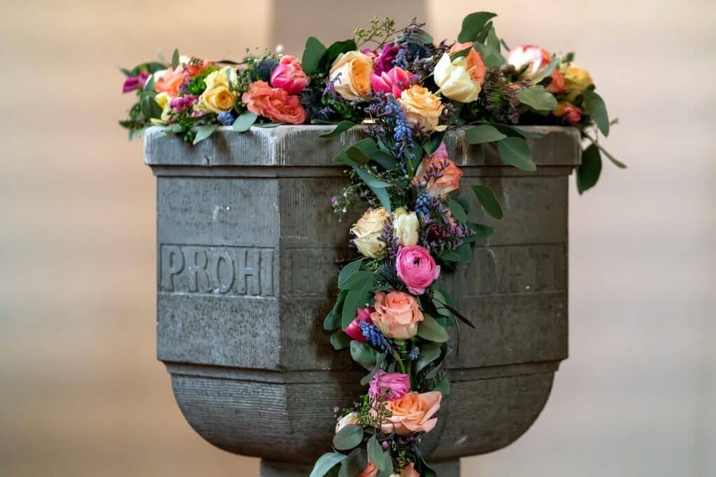 Bild von Hermann H. auf Pixabay, mit Blumen geschmückter Taufstein